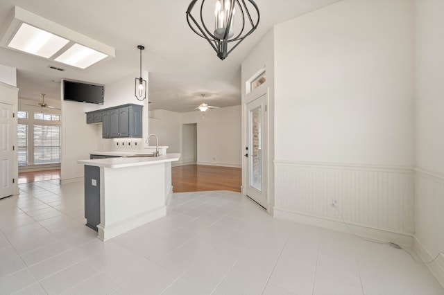 kitchen with a wainscoted wall, gray cabinetry, a sink, a peninsula, and light countertops