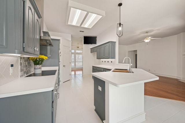 kitchen with gray cabinetry, a ceiling fan, a sink, backsplash, and black electric cooktop