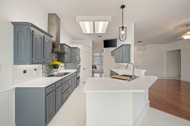 kitchen featuring a peninsula, island exhaust hood, a sink, light countertops, and black electric stovetop