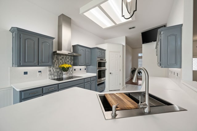 kitchen with stainless steel double oven, a sink, wall chimney exhaust hood, black electric cooktop, and tasteful backsplash