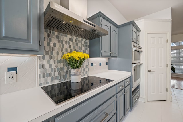 kitchen featuring black electric stovetop, light countertops, light tile patterned floors, stainless steel double oven, and wall chimney exhaust hood