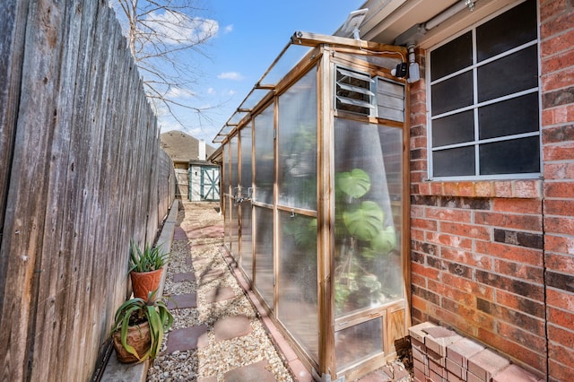 view of side of property with a greenhouse, an outbuilding, brick siding, and fence