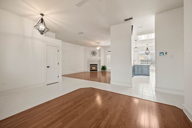 unfurnished living room featuring a ceiling fan, visible vents, light wood finished floors, a sink, and a tile fireplace