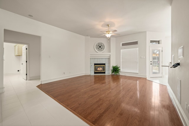 living room featuring baseboards, wood finished floors, ceiling fan, and a tile fireplace