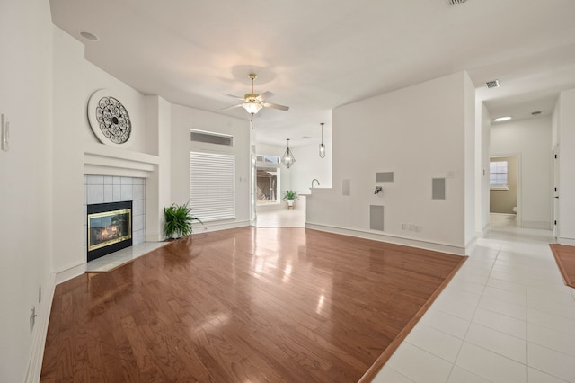 unfurnished living room with visible vents, baseboards, a tile fireplace, wood finished floors, and a ceiling fan