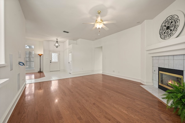 unfurnished living room featuring visible vents, baseboards, ceiling fan, a fireplace, and wood finished floors