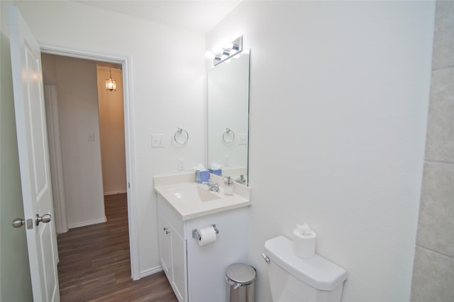 bathroom featuring toilet, baseboards, wood finished floors, and vanity