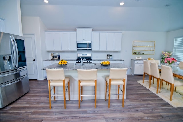 kitchen featuring white cabinetry, a kitchen bar, appliances with stainless steel finishes, and light stone counters