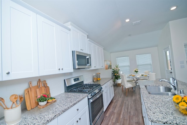 kitchen featuring white cabinets, decorative backsplash, wood finished floors, stainless steel appliances, and a sink