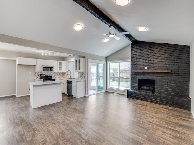 kitchen with a fireplace, stainless steel appliances, glass insert cabinets, open floor plan, and a sink