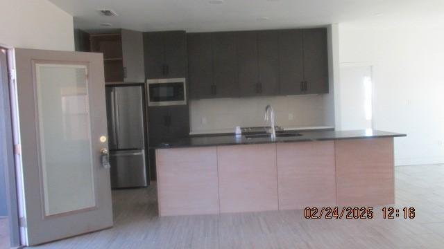 kitchen featuring dark countertops, appliances with stainless steel finishes, a sink, an island with sink, and modern cabinets