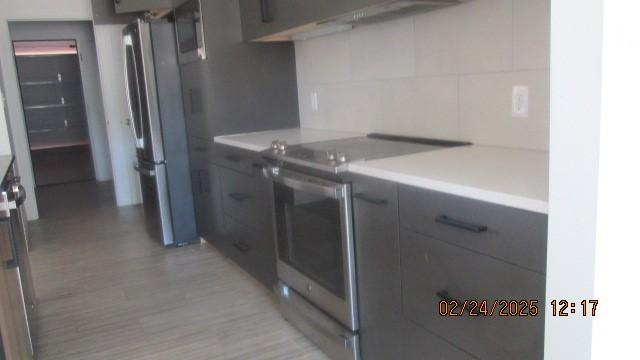 kitchen featuring decorative backsplash, modern cabinets, stainless steel appliances, light countertops, and gray cabinetry