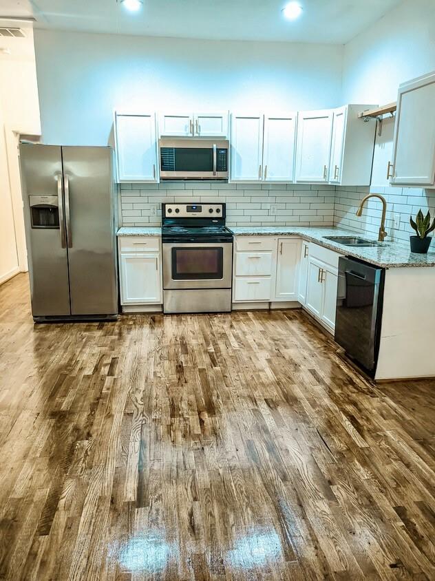 kitchen featuring dark wood finished floors, stainless steel appliances, decorative backsplash, white cabinets, and a sink