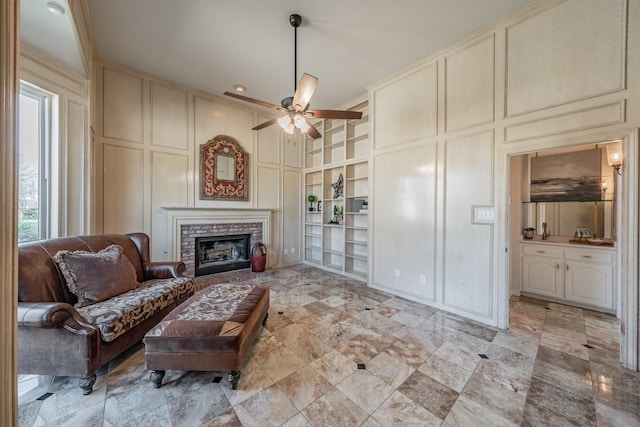 sitting room with ceiling fan, a decorative wall, built in features, ornamental molding, and a brick fireplace