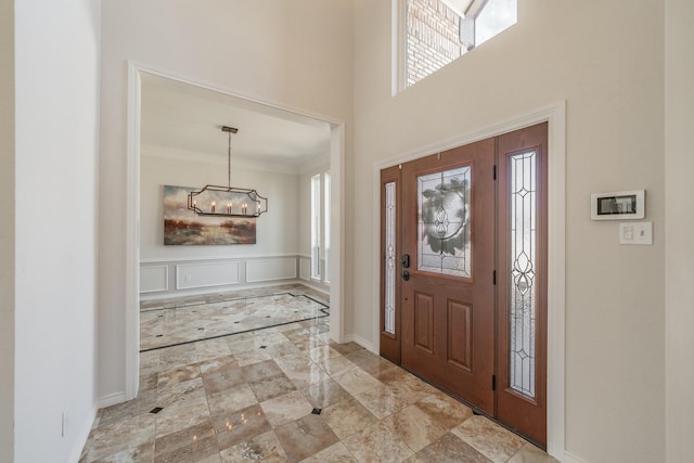 entrance foyer with baseboards, a towering ceiling, crown molding, a decorative wall, and a notable chandelier