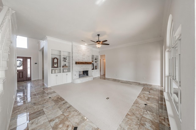 unfurnished living room with built in shelves, a large fireplace, ceiling fan, and ornamental molding