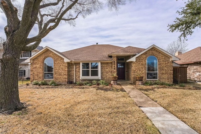 ranch-style home with a shingled roof, a front yard, and brick siding