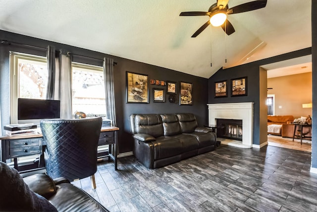 living area featuring a fireplace with raised hearth, ceiling fan, wood finished floors, baseboards, and vaulted ceiling