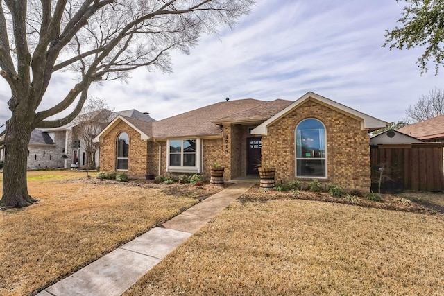 ranch-style home with roof with shingles, fence, a front lawn, and brick siding