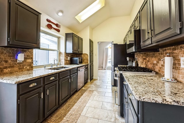 kitchen featuring vaulted ceiling with skylight, baseboards, appliances with stainless steel finishes, decorative backsplash, and light stone countertops