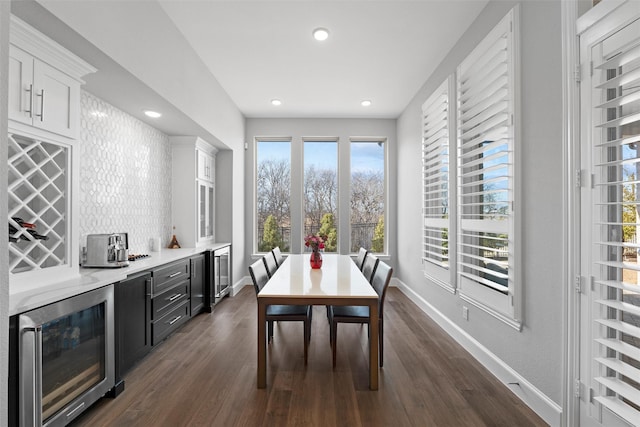 dining area featuring a bar, wine cooler, baseboards, and dark wood-type flooring