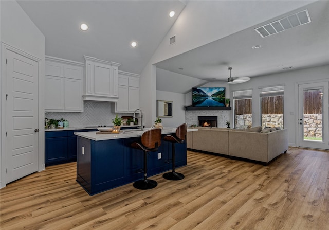 kitchen featuring visible vents, open floor plan, vaulted ceiling, light countertops, and a stone fireplace