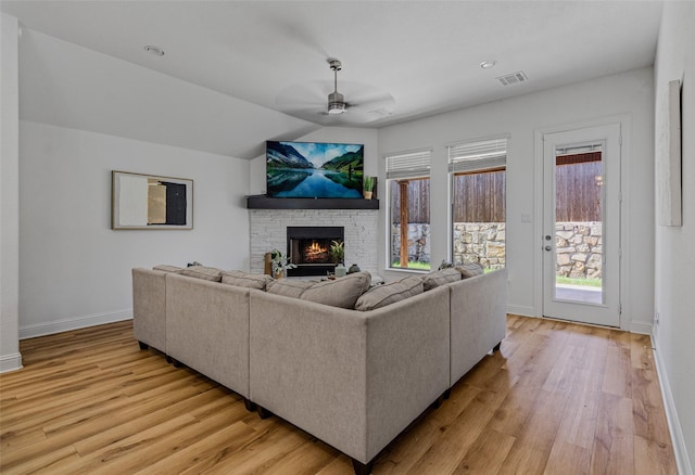 living room with a ceiling fan, a lit fireplace, light wood-style flooring, and baseboards