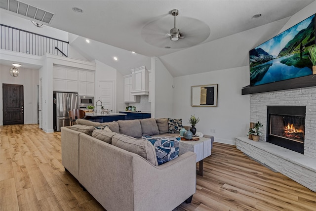 living area with a fireplace, visible vents, a ceiling fan, vaulted ceiling, and light wood finished floors