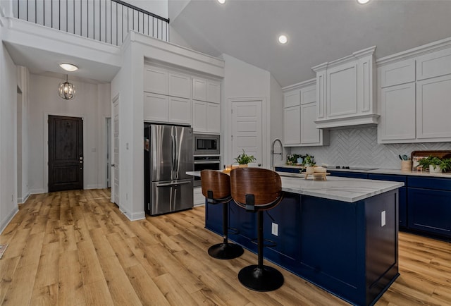 kitchen featuring a breakfast bar area, stainless steel appliances, backsplash, light wood finished floors, and a center island with sink