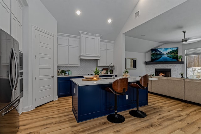 kitchen with open floor plan, vaulted ceiling, light countertops, a stone fireplace, and black appliances