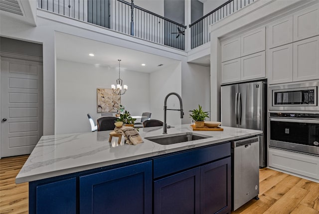 kitchen with a notable chandelier, a center island with sink, appliances with stainless steel finishes, a sink, and blue cabinets