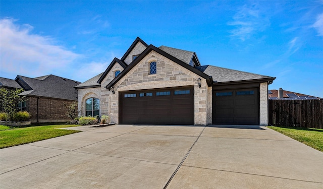 french provincial home featuring an attached garage, a shingled roof, fence, driveway, and stone siding