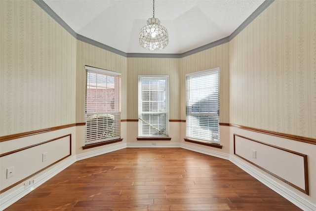 empty room featuring wallpapered walls, wainscoting, lofted ceiling, wood-type flooring, and a textured ceiling