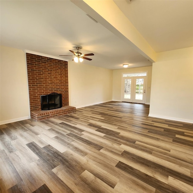 unfurnished living room featuring wood finished floors, a ceiling fan, baseboards, french doors, and a brick fireplace