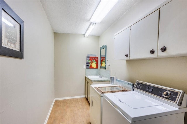 washroom featuring cabinet space, a sink, a textured ceiling, light wood-type flooring, and washer and dryer