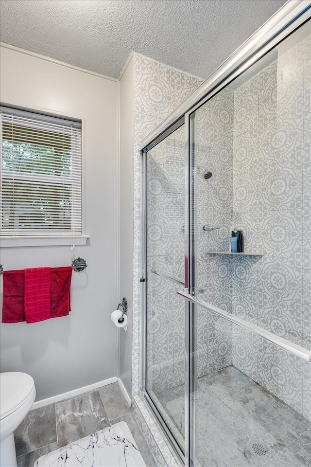 bathroom with baseboards, a shower stall, toilet, and a textured ceiling