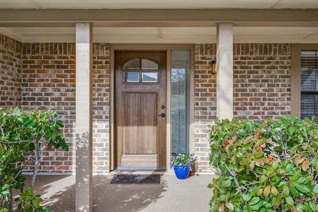 doorway to property with a porch and brick siding