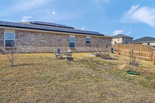 back of house featuring roof mounted solar panels, brick siding, a lawn, and fence