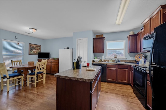 kitchen with a sink, a kitchen island, visible vents, light wood-style floors, and black appliances