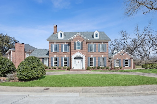 georgian-style home featuring a chimney, a front lawn, and brick siding