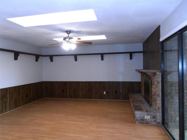 basement featuring a wainscoted wall, ceiling fan, a brick fireplace, and light wood finished floors