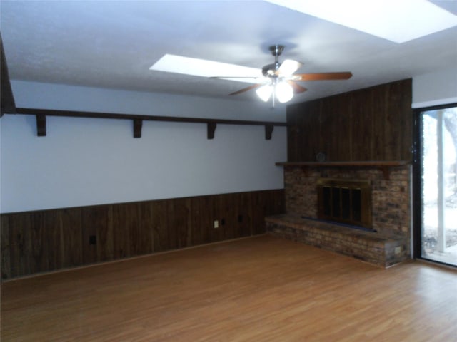 unfurnished living room featuring plenty of natural light, wainscoting, a skylight, and a fireplace