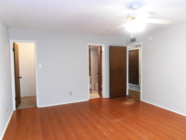 unfurnished bedroom with connected bathroom, wood finished floors, visible vents, and baseboards