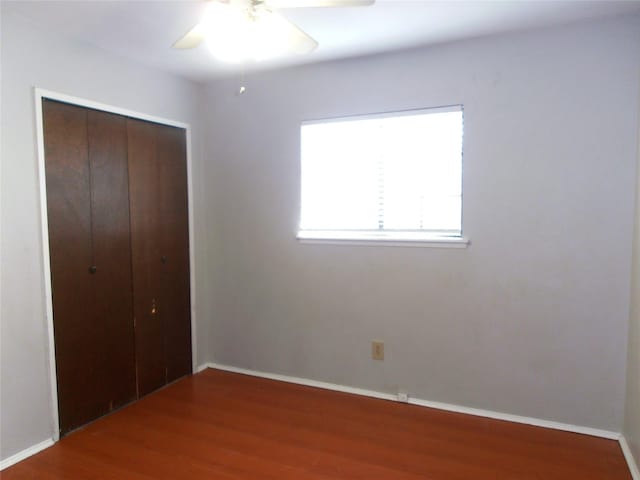 unfurnished bedroom featuring a ceiling fan, baseboards, a closet, and wood finished floors