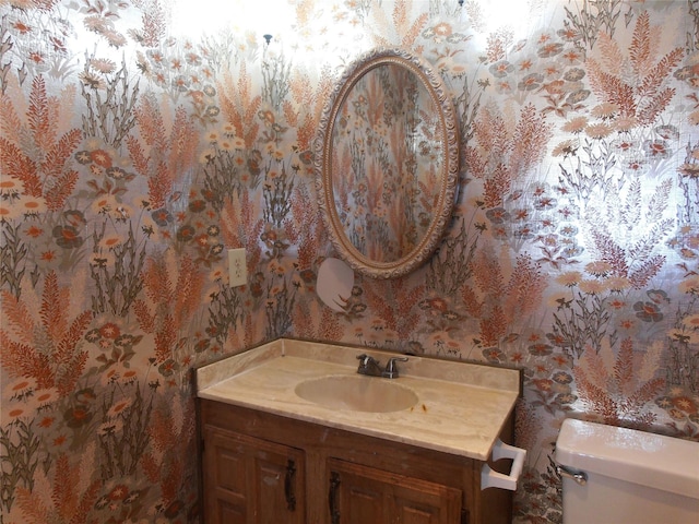 half bathroom with vanity, toilet, and wallpapered walls