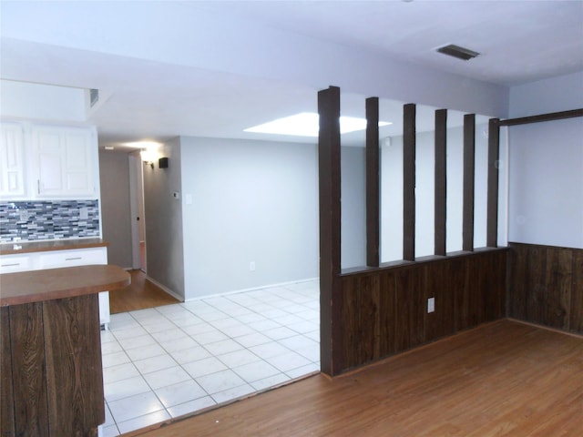 empty room with light wood-type flooring, wood walls, visible vents, and wainscoting