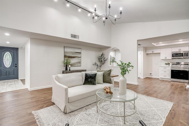 living area with high vaulted ceiling, visible vents, light wood-style flooring, and baseboards