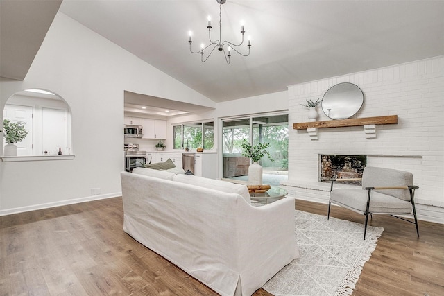 living room featuring high vaulted ceiling, a notable chandelier, a fireplace, baseboards, and light wood-type flooring