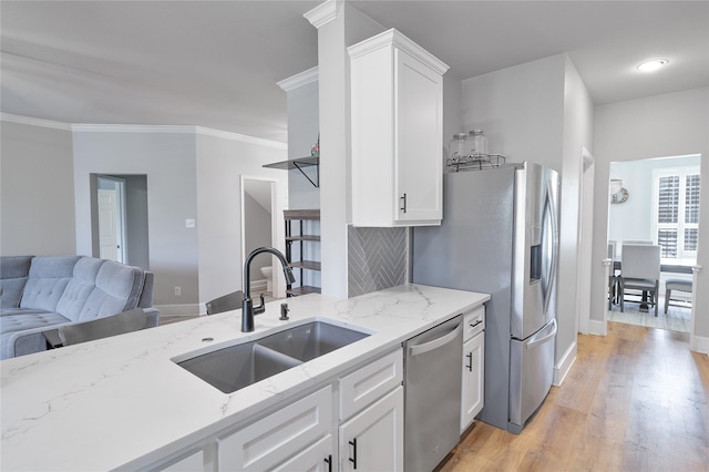 kitchen with white cabinets, light stone counters, appliances with stainless steel finishes, light wood-style floors, and a sink