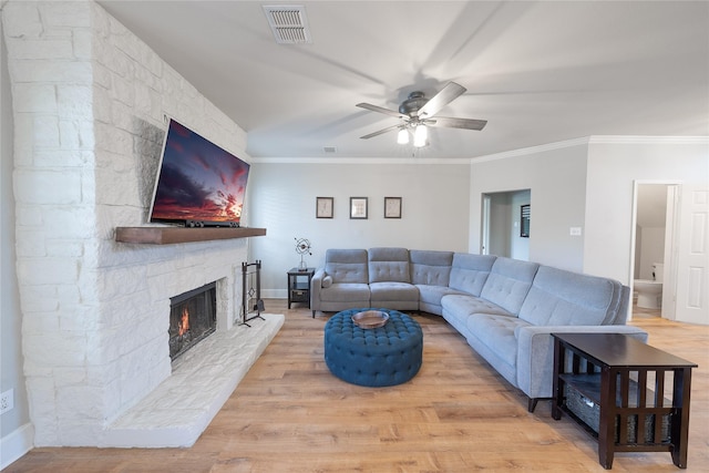 living room with crown molding, a fireplace, visible vents, ceiling fan, and wood finished floors